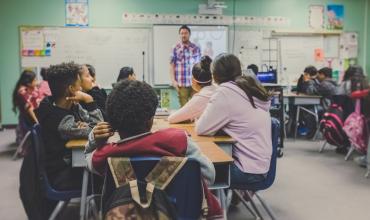 Kids in a classroom with a teacher in front of the dry erase board