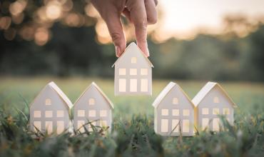 A paper house being placed on grass by a hand