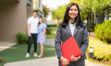 a real estate agent standing in the foreground with a couple standing together in the background