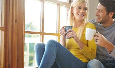 a young couple sitting on a windowsill, smiling and drinking coffee