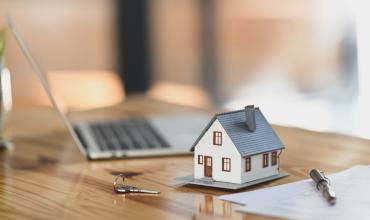 Miniature house beside a keyboard and paperwork on desk