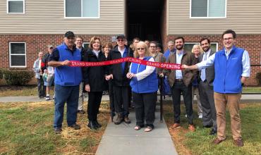 A group of people cutting a ribbon outside of the apartment development