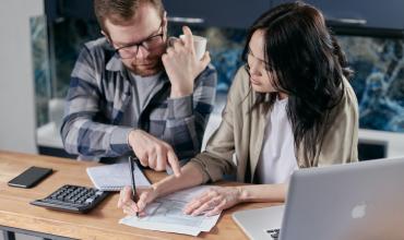 Two people calculating things on a notepad and laptop