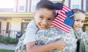 Veteran Homelessness is Decreasing in North Carolina A child holding the US flag being held by their parent in military uniform