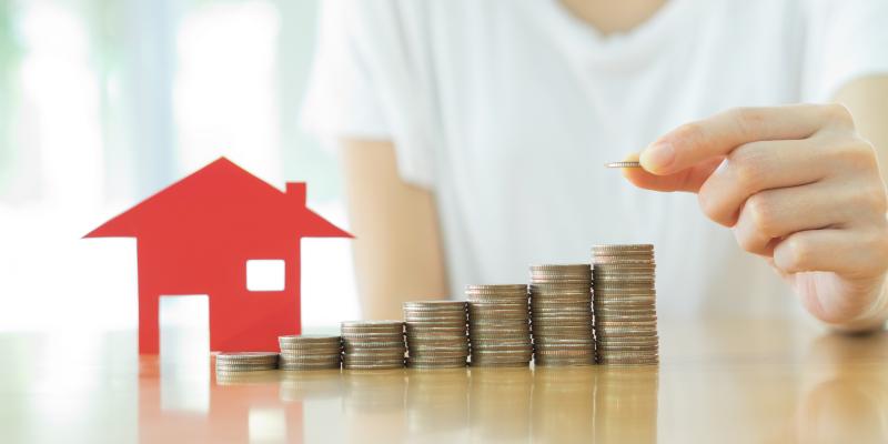 Small red house with stacks of coins next to it on a counter with a person behind it