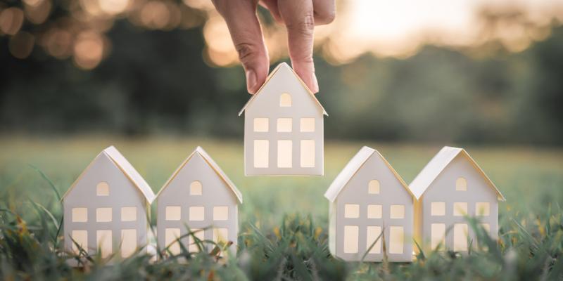 A paper house being placed on grass by a hand