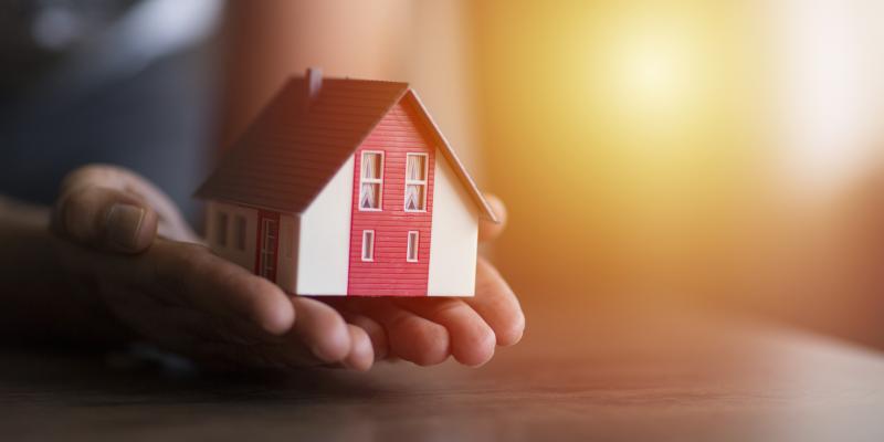 Person holding a small house in their hands over a desk