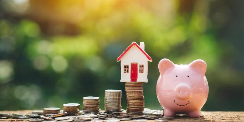 A piggy bank with change and a little house on a desk