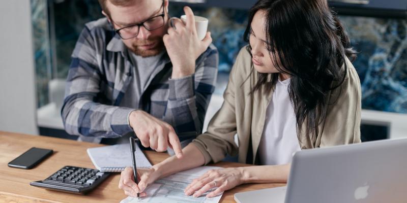 Two people calculating things on a notepad and laptop